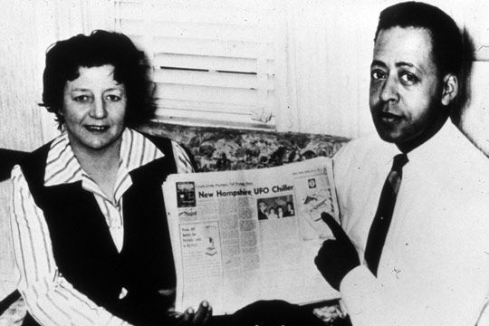 Betty and Barney Hill holding a newspaper featuring a story about their abduction experience.