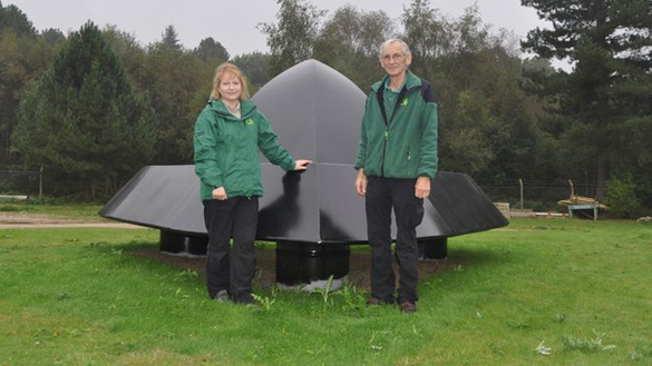 The Rendlesham UFO sculpture. Standing in front of it are artist Olivia English and Rendlesham Forest Recreation Manager Nigel Turner. (Credit: BBC)
