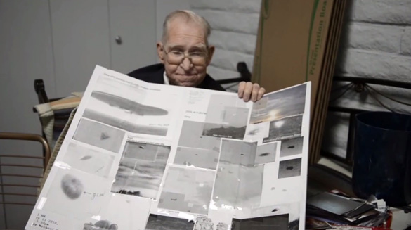 Bushman with a display of alleged UFO pictures from Area 51. (Credit: YouTube/Mark Q Patterson)
